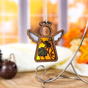 A charming Festive Pumpkin Ornament from Forged Flare® hangs from a white string, featuring a 3.5" wooden angel figurine with an orange body adorned with an embossed leaf and acorn design. Set against a blurred, autumn-themed background filled with warm tones and foliage, this delightful piece from the Mother's Angels® collection makes for a perfect fall decoration or thoughtful memorial gift.