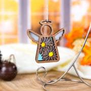 A 3.5" Mother’s Angels® Daisy Ornament by Forged Flare®, featuring cut-out wings and two daisies, hangs from a string. The softly blurred background shows a window and autumn decor, as displayed on Amazon.