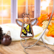 A Forged Flare® Mother's Angels® Swallowtail Butterfly Ornament—3.5" angel figurine with painted wings and yellow-black butterflies—hangs on a stand, autumn leaves and pinecones nearby. A unique collector’s item or Amazon marketplace find.