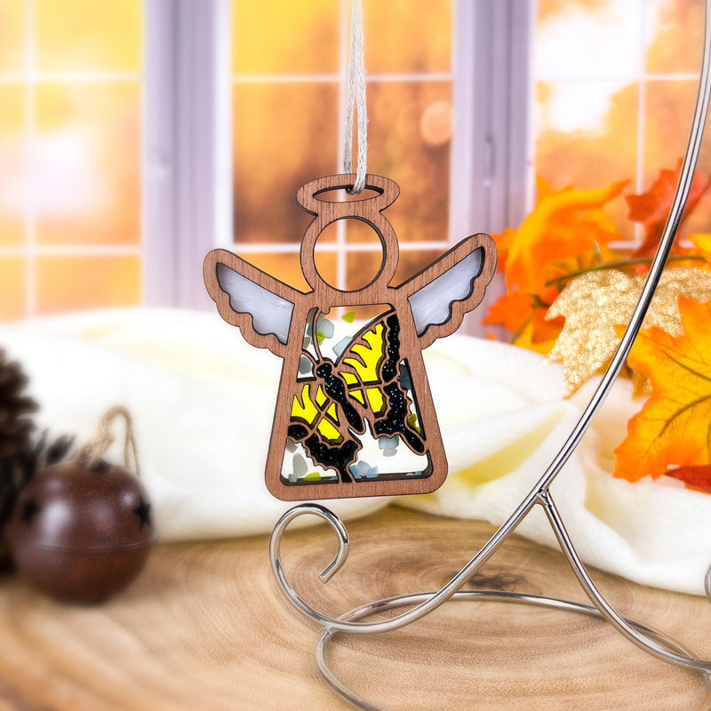 A Forged Flare® Mother's Angels® Swallowtail Butterfly Ornament—3.5" angel figurine with painted wings and yellow-black butterflies—hangs on a stand, autumn leaves and pinecones nearby. A unique collector’s item or Amazon marketplace find.