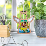 The Forged Flare® Ladybug and Dandelion Ornament is a 3.5" Mother's Angels® figurine featuring a wooden angel with white wings, a bright ladybug, and yellow dandelions—an adorable accent for your space.