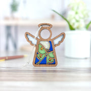The Forged Flare® Luna Moth Ornament, a 3.5" Mother's Angels® wooden angel figurine, stands on a light wooden surface with softly blurred potted plant and pen in the background.