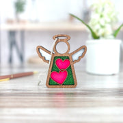 The Limited Edition Interlocking Hearts Ornament - Series 8 by Forged Flare® features a 3.5" wooden Mother's Angels® angel with interlocking hearts and green glitter, perfect for cozy holiday decor or your Christmas tree ornament collection.