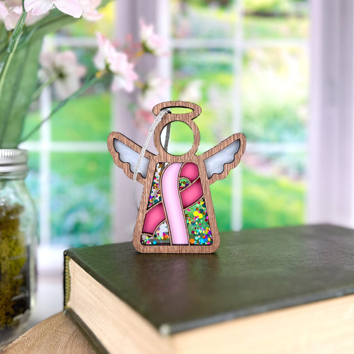 A pink ribbon angel ornament rests on a book, a meaningful gift symbolizing hope and support for breast cancer awareness.