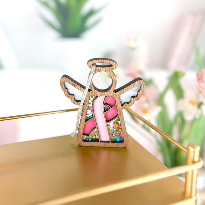 Elegant ornament with a pink ribbon for breast cancer awareness, displayed on a golden shelf with a soft backdrop.