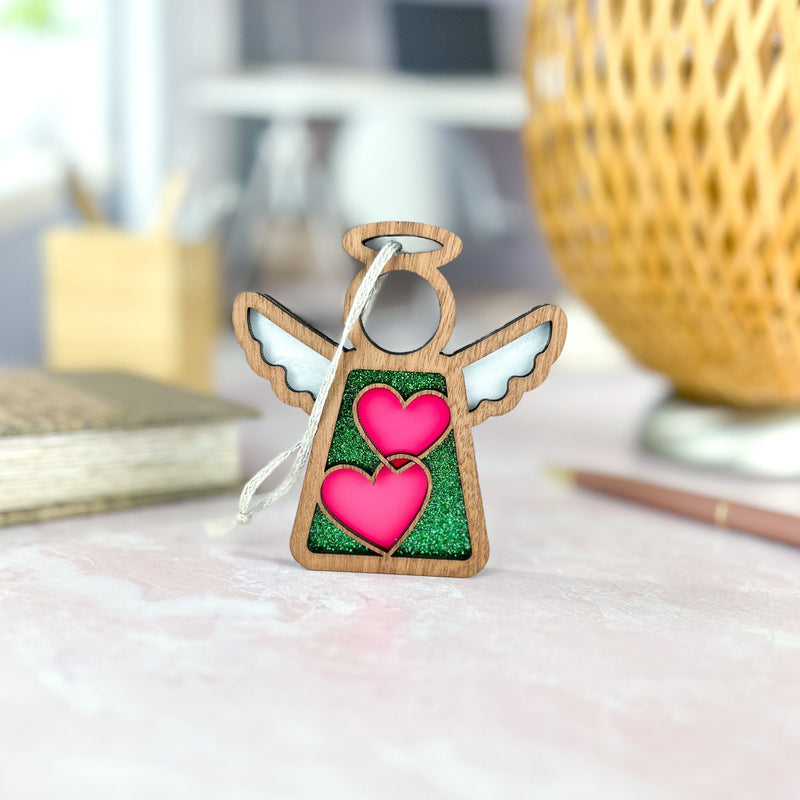 The Forged Flare® Limited Edition Interlocking Hearts Ornament - Series 8 is a 3.5" wooden Mother's Angels® figurine with white wings, green glitter center, and pink interlocking hearts, perfect as a festive Christmas tree ornament.