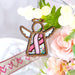 A pink ribbon angel ornament, nestled among flowers, is a beautiful gift for breast cancer patients and survivors for awareness.