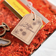The Forged Flare® Gift Tag - "For You. Just Because.", 3" (H), features floral decorations and is attached to a gift box containing orange shredded paper.