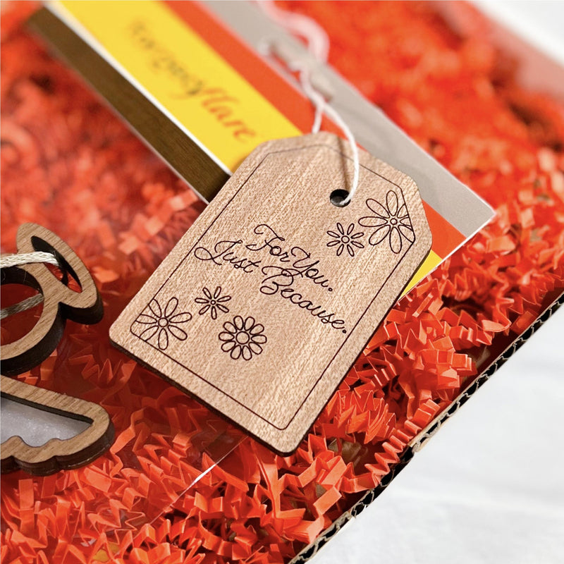 The Forged Flare® Gift Tag - "For You. Just Because.", 3" (H), features floral decorations and is attached to a gift box containing orange shredded paper.