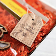 A Forged Flare® "Happy Birthday" gift tag (3" H) with flower designs decorates a package filled with orange crinkle paper.