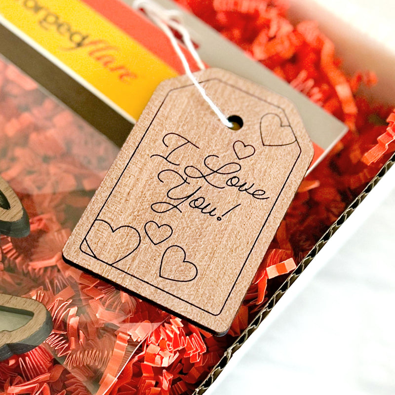 The Forged Flare® Gift Tag - "I Love You!", 3" (H) features engraved hearts and a loving message, presented on red shredded paper in a gift box.