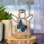 The Forged Flare® Warehouse Return - Morpho Blue Butterfly Ornament features a 3.5" Mother's Angels® wooden angel with a glittery blue butterfly—ideal for cozy décor and fans of unique finds.