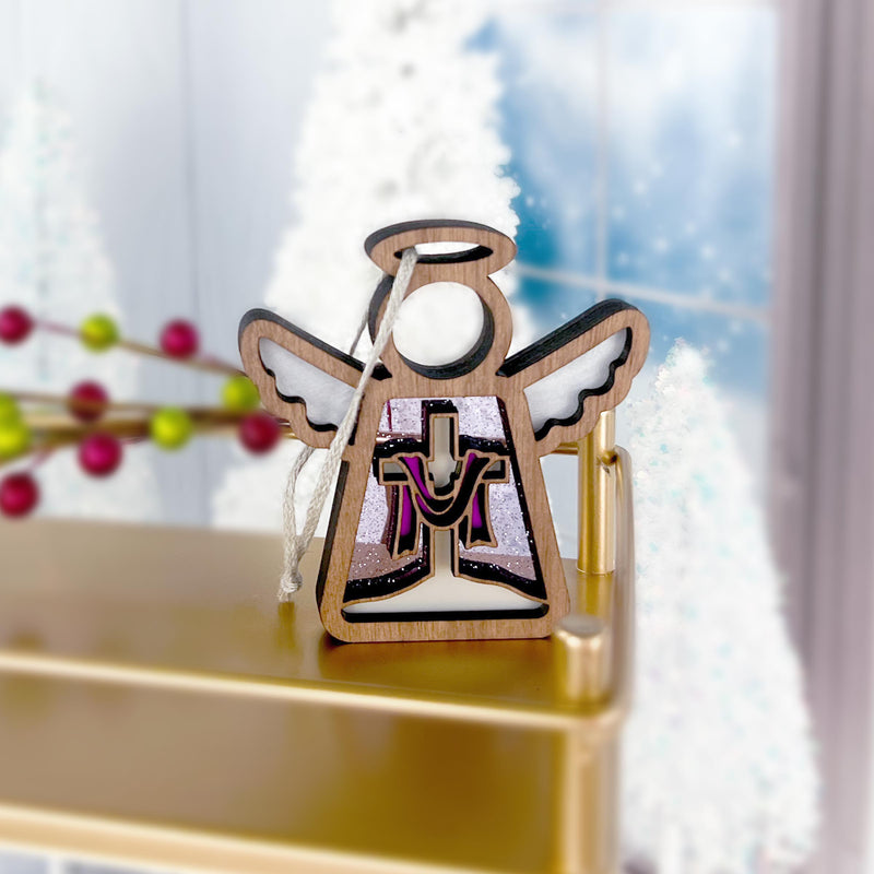 The Limited Edition By Grace Ornament, a 3.5" Angel Figurine from Mother's Angels® by Forged Flare®, stands on a gold-colored surface. The wooden angel ornament features intricate cut-out designs and stained glass accents. The background showcases a frosty window and holiday decorations with red and green berries, evoking a festive and wintery atmosphere, perfect as an Easter gift.