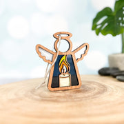 The Forged Flare® Mother's Angels® Burning Candle Ornament is a 3.5" wooden angel figurine with a stained glass-style candle, ideal as a Christmas decoration or memorial gift. Shown on wood with a blurred background and green plant.
