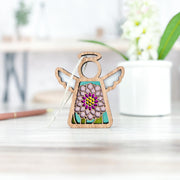 The Forged Flare® Chrysanthemum Ornament with Imperfections is a 3.5" handcrafted wooden angel figurine featuring pink and purple mums—a unique Mother's Angels® collectible perfect for display on any table.