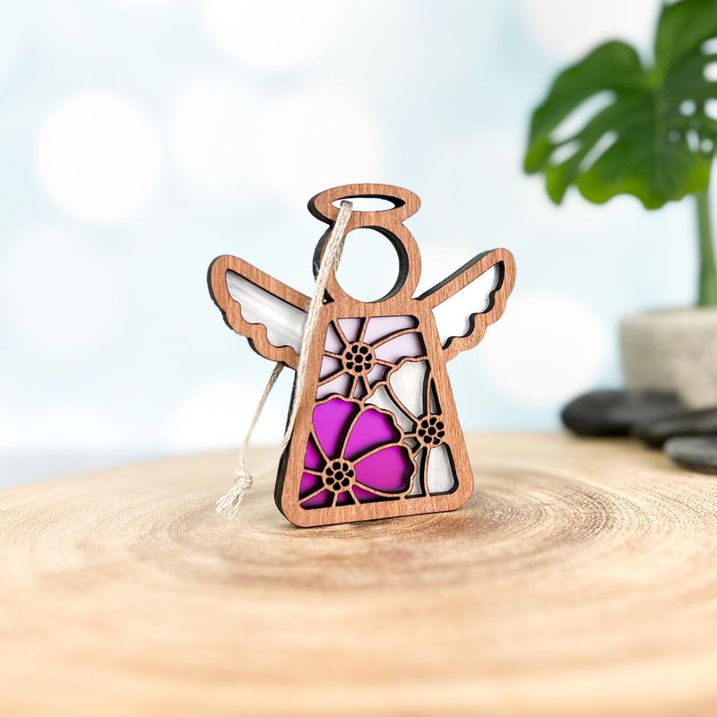 The Forged Flare® Cosmos Ornament | 3.5" (H) Angel Figurine from Mother's Angels® features stained glass-style wings with purple, pink, and white cosmos flower designs and hangs by a string, displayed against a green plant backdrop.