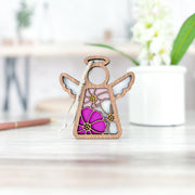The Forged Flare® Cosmos Ornament | 3.5" (H) Angel Figurine from the Mother's Angels® collection features stained-glass-style pink and purple cosmos flowers, displayed on a light wooden surface with a blurred floral pot in the background.