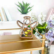 The Forged Flare® Daffodil Ornament | 3.5" (H) Angel Figurine from the Mother's Angels® collection sits on a gold shelf with books and plants—an ideal birth flower gift for bright, modern spaces.