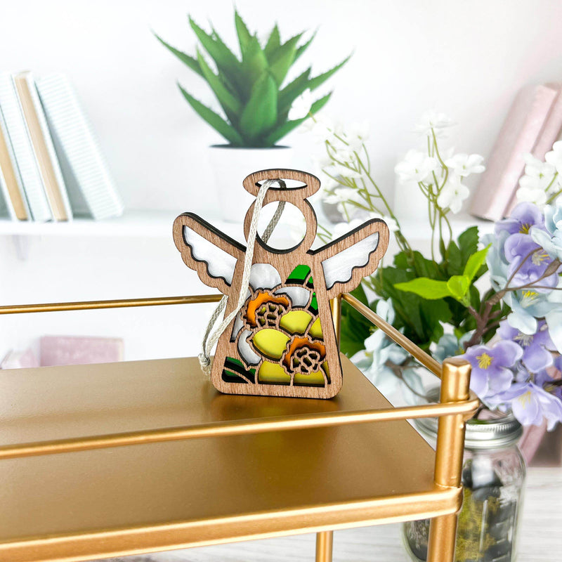 The Forged Flare® Daffodil Ornament | 3.5" (H) Angel Figurine from the Mother's Angels® collection sits on a gold shelf with books and plants—an ideal birth flower gift for bright, modern spaces.