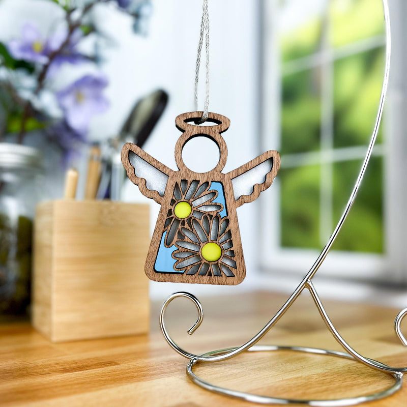 The Warehouse Return - Daisy Ornament (3.5" H) by Forged Flare®, from the Mother's Angels® collection, features cutout wings, two daisies, and a blue background—perfectly displayed on a metal stand for the Amazon marketplace.