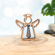 The Forged Flare® Forever Your Father Ornament, a 3.5" Mother's Angels® figurine with halo and wings, stands on a tree slice—making it a heartfelt Father's Day gift or Christmas ornament, softly framed by blurred green in the background.
