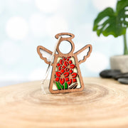 The Forged Flare® Gladiolus Ornament | 3.5" (H) Mother's Angels® features a wooden angel figurine with a red gladiolus flower design, white hanging string, and is displayed on a round wooden surface with green plants and gray stones in the background.