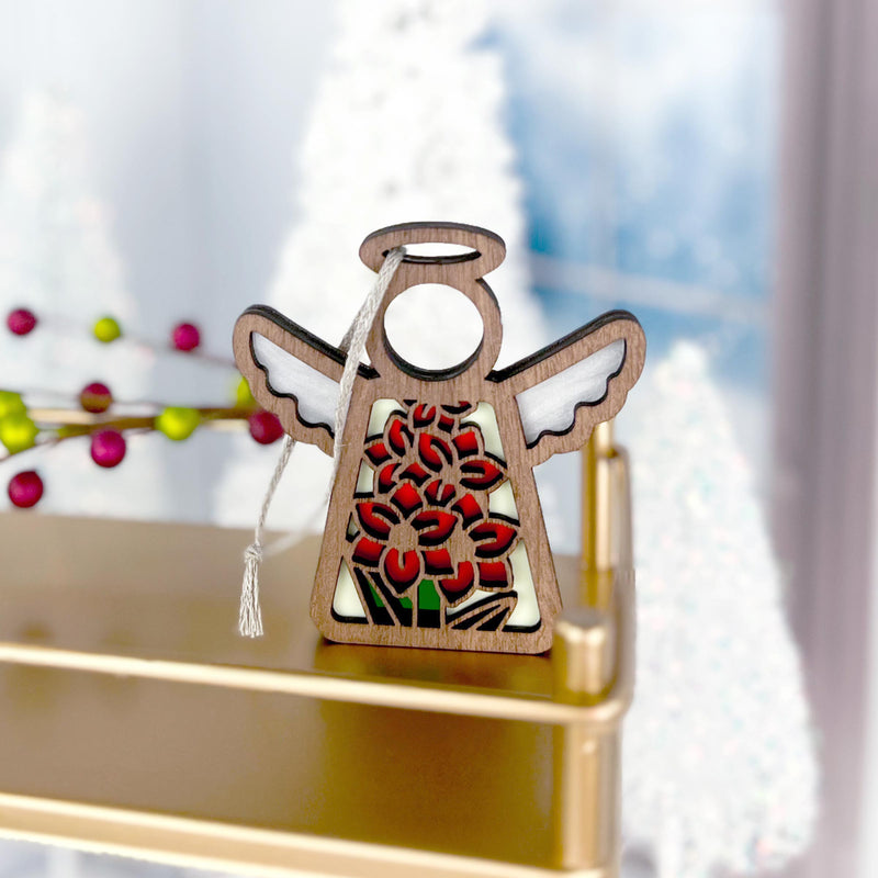 The Forged Flare® Gladiolus Ornament is a 3.5" wooden angel figurine from the Mother's Angels® collection, featuring a cut-out gladiolus flower and green leaves, displayed on a gold shelf with festive decor in the background.