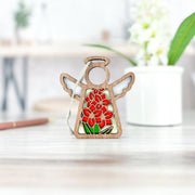 The Forged Flare® Gladiolus Ornament | 3.5" (H) Angel Figurine from the Mother's Angels® collection features an August birth flower design and stands on a light wooden surface, with a white potted plant blurred in the background.