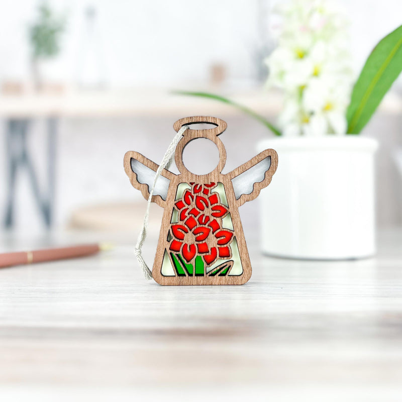 The Forged Flare® Gladiolus Ornament | 3.5" (H) Angel Figurine from the Mother's Angels® collection features an August birth flower design and stands on a light wooden surface, with a white potted plant blurred in the background.