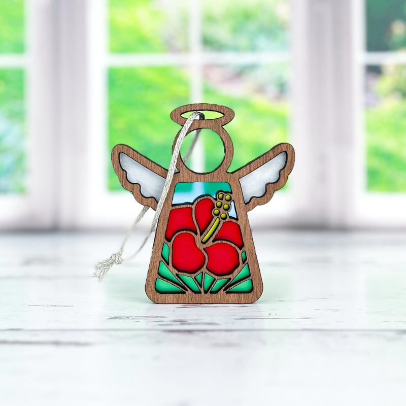 The Hibiscus Ornament | 3.5" Angel Figurine from Mother's Angels® by Forged Flare® is depicted against a vibrant backdrop. This gorgeous angel features red hibiscus flowers at its center, green accents at the base, pristine white wings, and a circular halo. A string is attached to make it easy for hanging on your Christmas tree.