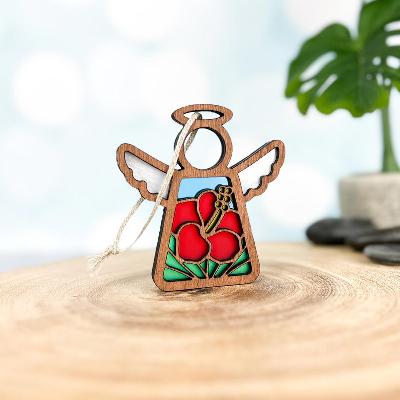 The Forged Flare® Hibiscus Ornament is a 3.5"H Mother's Angels® angel figurine with wings and a painted red hibiscus flower, featuring a hanging string and displayed on a wooden surface.