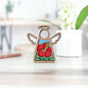 The Forged Flare® Hibiscus Ornament | 3.5" (H) Angel Figurine from the Mother's Angels® collection features stained glass-style red hibiscus flowers and green leaves, displayed on a light wooden surface with a blurred floral pot in the background.