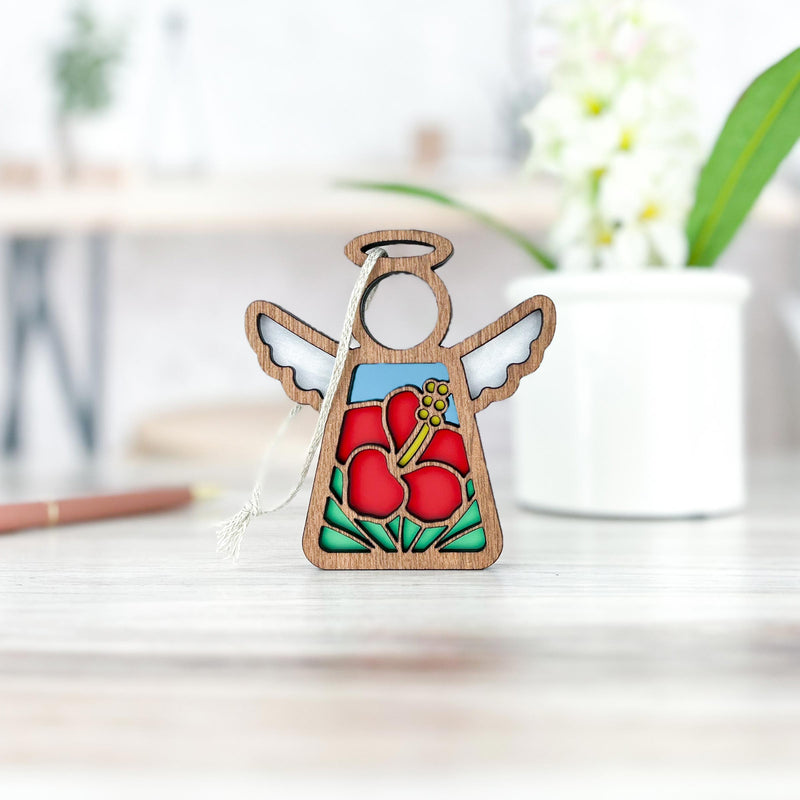 The Forged Flare® Hibiscus Ornament | 3.5" (H) Angel Figurine from the Mother's Angels® collection features stained glass-style red hibiscus flowers and green leaves, displayed on a light wooden surface with a blurred floral pot in the background.