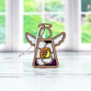 The Forged Flare® Mother's Angels® Jonquil Ornament is a 3.5" wooden angel figurine with stained glass-style wings and a jonquil flower, perfect for March birthdays, shown on a white surface before a sunlit window.