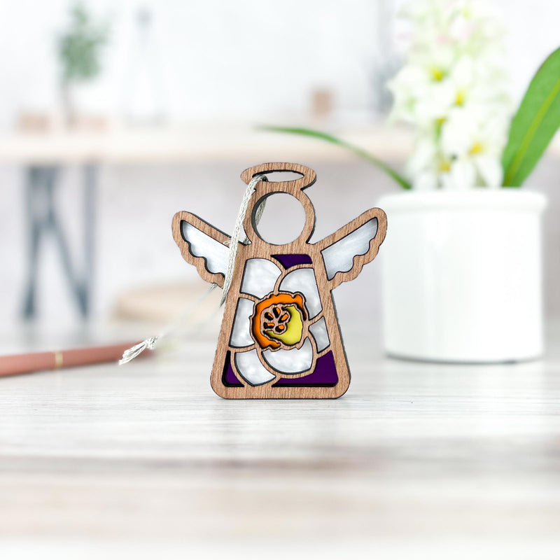 The Forged Flare® Mother's Angels® Jonquil Ornament is a 3.5" wooden angel figurine featuring March’s white jonquil bloom with an orange center, displayed on light wood with blurred greenery in the background.