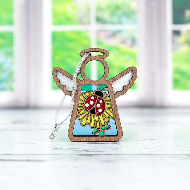 The Forged Flare® Ladybug and Dandelion Ornament is a 3.5" Mother's Angels® angel figurine with white wings, featuring a colorful ladybug on a yellow flower, and includes a silver hanging string—perfect for any bright window.