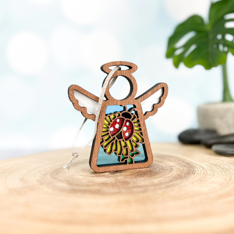 The Forged Flare® Mother's Angels® Ladybug and Dandelion Ornament is a 3.5" wooden angel figurine featuring colorful ladybug and dandelion details—perfect as a Christmas tree ornament or decorative accent.