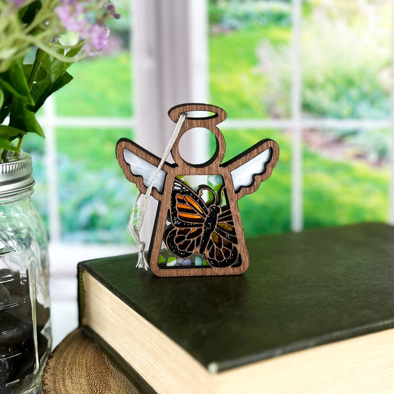 The 3.5" Monarch Butterfly Ornament with Imperfections from Mother's Angels® by Forged Flare® stands on a book beside a mason jar and flowers—sunlit, evoking warmth and remembrance as an ideal memorial gift.