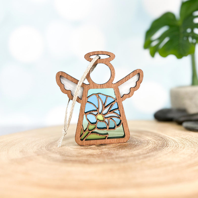 The Forged Flare® Morning Glory Ornament is a 3.5" wooden Mother's Angels® figurine with cutout wings, a halo, and a blue stained-glass style September birth flower design, shown on wood with blurred greenery behind.