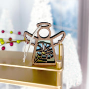 The Forged Flare® Morning Glory Ornament is a 3.5" angel figurine from the Mother's Angels® collection, featuring blue morning glory flowers and a hanging string, displayed on a gold shelf with festive décor in the background.