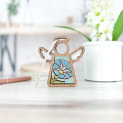 The Forged Flare® Morning Glory Ornament, a 3.5" Mother's Angels® figurine featuring September’s birth flower, stands on a light surface with a hanging white string. A white potted plant and blurred background complete the scene.