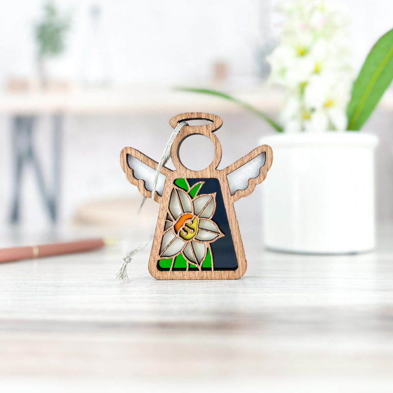 The Forged Flare® Narcissus Ornament | 3.5" (H) Angel Figurine from Mother's Angels® features a white narcissus and green leaves design, displayed on a light wood surface—ideal as a December birth flower keepsake.