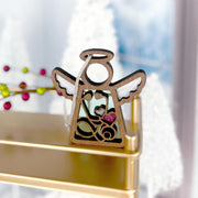 A 3.5" Mother's Angels® Doctor/Nurse ornament by Forged Flare®, featuring angel figurine details with imperfections, displayed on a gold shelf with festive decorations and trees blurred in the background.