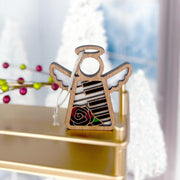 The Piano & Rose Ornament with Imperfections by Forged Flare® is a 3.5" handcrafted Mother's Angels® figurine featuring black and white piano keys and a red rose, displayed on a gold shelf with festive decor in the background.