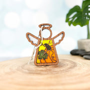 Displayed on a circular wood slice, the Festive Pumpkin Ornament (3.5" Angel Figurine) by Forged Flare® from Mother's Angels® features a small wooden angel with white wings and a halo. The angel's body is adorned with an autumn leaf and pumpkin design. A green plant with large leaves is blurred in the background, making this piece perfect as a memorial gift or Thanksgiving decor.