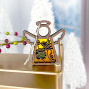 A beautiful Festive Pumpkin Ornament from the Mother's Angels® collection by Forged Flare®, featuring a 3.5" angel figurine with wings and a body adorned with fruits, including a pineapple and grapes. The ornament is set against a golden surface with blurred Christmas decorations and white trees in the background, making it an ideal addition for both Thanksgiving decor and as a charming Christmas tree ornament.