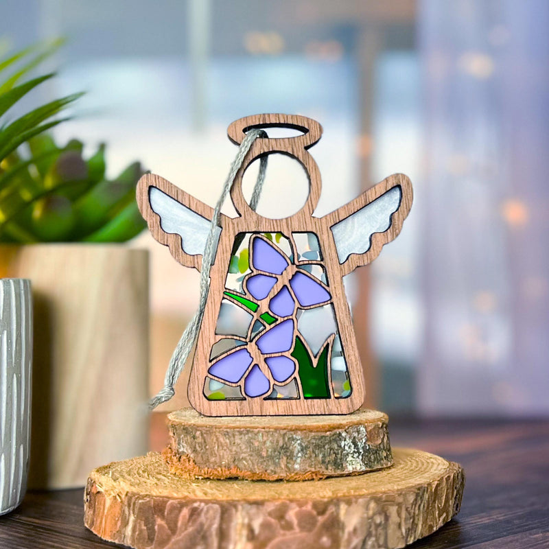 The Forged Flare® Mother's Angels® 3.5" Playful Purple Butterflies Ornament stands on stacked tree slices, with a potted plant in the blurred background—ideal as a gift and available as a Warehouse Return on Amazon.