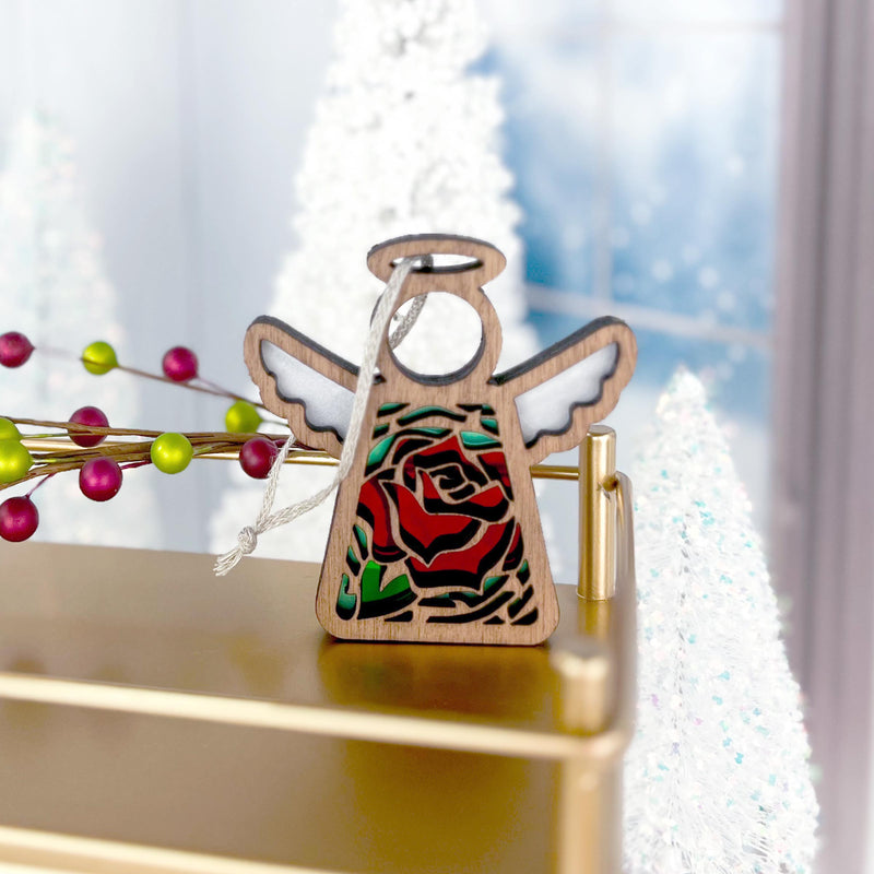 The 3.5" Red Rose Ornament with Imperfections angel figurine from Mother's Angels® by Forged Flare® stands on a gold surface, surrounded by white Christmas trees and berry decorations in a festive holiday scene.