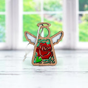 The Forged Flare® Mother's Angels® Red Rose Ornament with Imperfections is a 3.5" wooden angel figurine, featuring a stained glass-style red rose centerpiece and green leaves, hanging by a silver string.