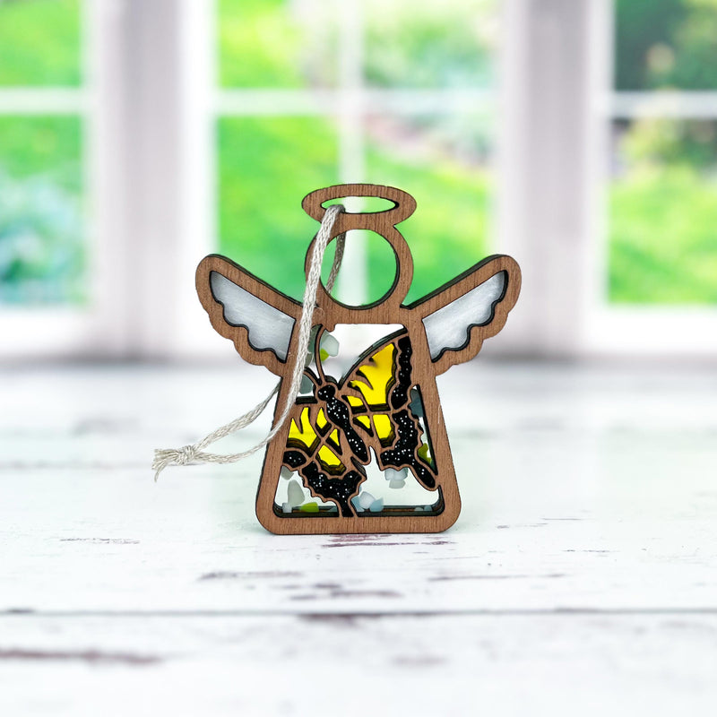 The 3.5" Mother's Angels® Swallowtail Butterfly Ornament by Forged Flare® stands ready to hang on a white surface, white wings and yellow butterfly design glowing with a garden view behind. Find this warehouse return on Amazon.